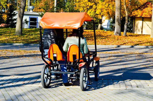 La gente monta una bicicleta de cuatro ruedas naranja de moda, una tarjeta de bicicleta con una rueda en el parque de otoño
 - Foto, Imagen