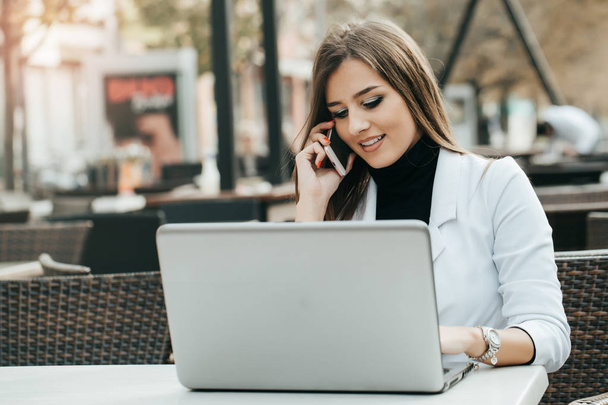 Счастливая современная и привлекательная предпринимательница, работающая с телефоном и ноутбуком в кафе на улице
 - Фото, изображение