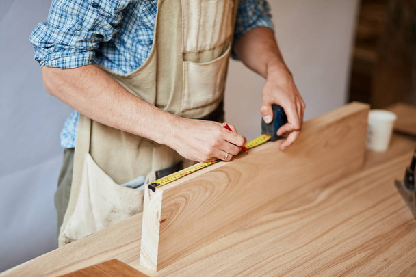 hand of a carpenter taking measurement of a wooden plank - Foto, imagen