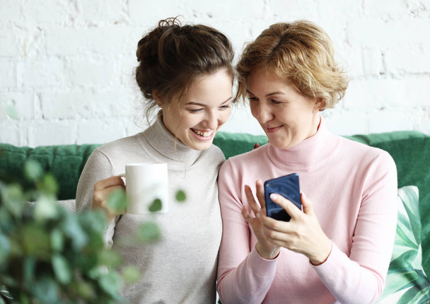 Family, people and technology. Aged woman and her adult daughter using smartphone at home. - Foto, Bild