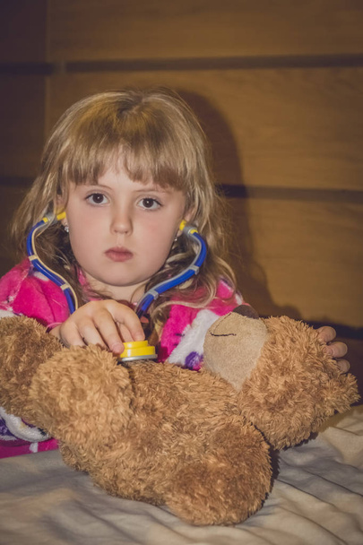 Cute Little Caucasian girl playing Doctor with her favourite teddy bear - Photo, Image