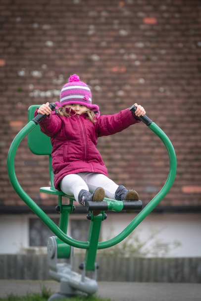 Little Caucasian girl exercising on the outdoor training machine on a chilly autumn day - Photo, Image