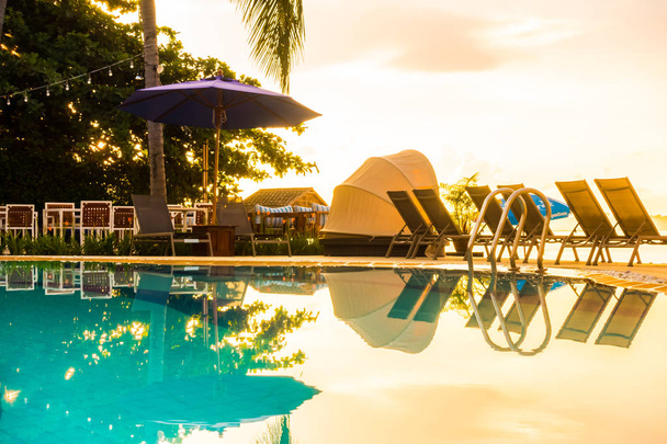 Krásné venkovní pohled s deštníkem a židle kolem bazénu v luxusní hotel a letovisko v době východu slunce pro cestování a dovolenou - Fotografie, Obrázek