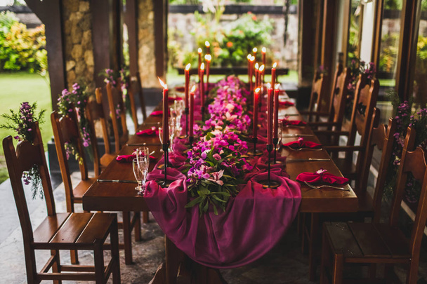 Mesa de boda de madera decorada con velas rojas, tela rosa y orquídeas púrpuras
 - Foto, Imagen