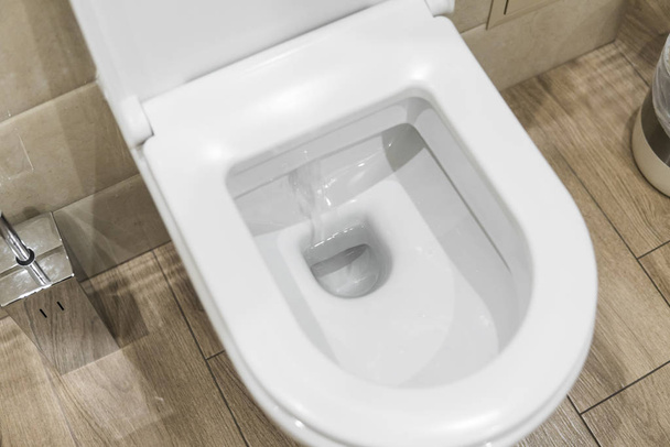 White toilet bowl in a bathroom. Closeup view of a flushing white toilet. The water swirls in the toilet bowl. - Valokuva, kuva