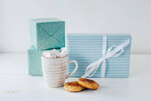 Taza llena de malvaviscos en la mesa con galletas y regalos azules
 - Foto, Imagen