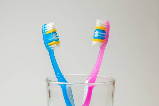 Two denture pink and blue in glass on gray background. The concept of toothbrushes for couple, joint residence  - 写真・画像