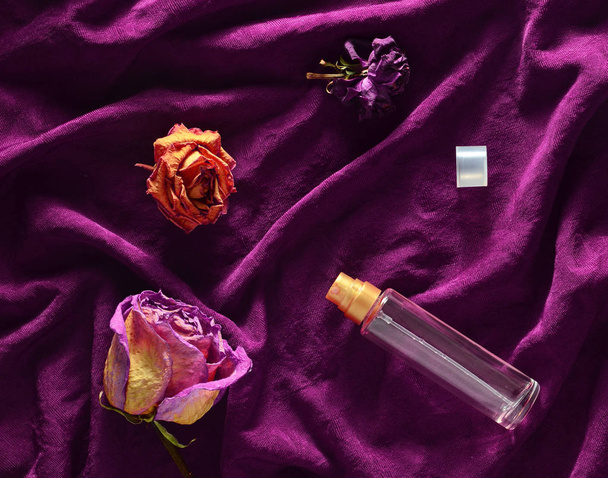 Ένα μπουκάλι του αρώματος και μπουμπούκια από αποξηραμένα τριαντάφυλλα σε φόντο κόκκινο μετάξι. Το ρομαντικό βλέμμα. Το Top view. - Φωτογραφία, εικόνα