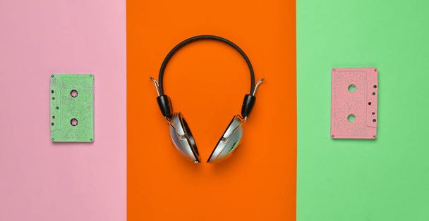 Vezeték nélküli fejhallgató és a színes pasztell papír alapon audio kazetták. Minimális creative art. Zenei retro rezgéseket. Szemközti nézet - Fotó, kép