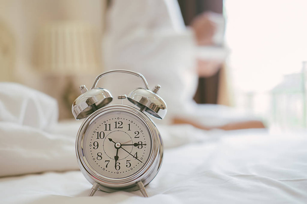 Éjjeli Alarm clock állva már a harang kora reggel felébredni nő az ágyban, háttérben a streching. Pihentető koncepció. - Fotó, kép