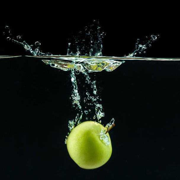 Green apple under water against black background  - 写真・画像