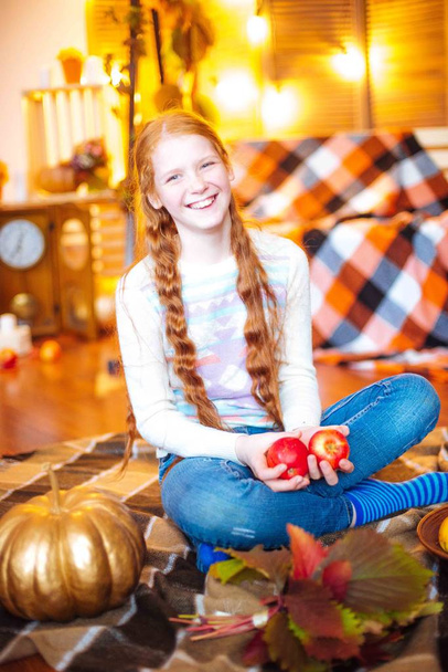 Red-haired teenager girl in a studio in the fall scenery with yellow leaves and apples - Photo, Image