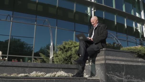 Old man is working with laptop in the city - Materiał filmowy, wideo