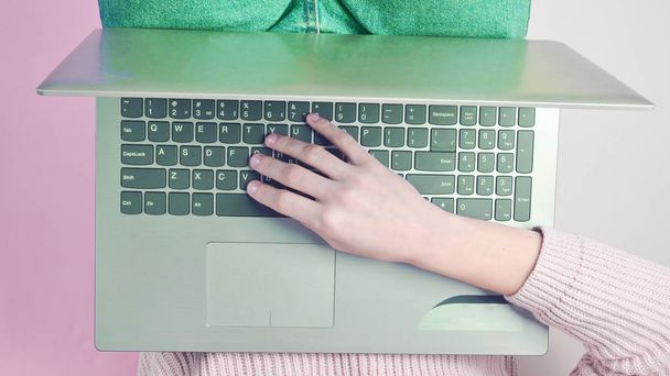 Het meisje is het typen op het toetsenbord van de laptop. Trend van minimalisme. Online werken, freelancen, bloggen. Bovenaanzicht op een pastel achtergrond. - Foto, afbeelding