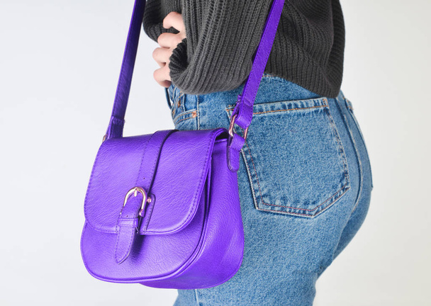 Girl in fit jeans, sweater and with bag on the odds posing on white background. Side view. - Photo, Image
