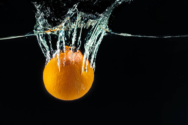 Orange falling into water and making splashes - Фото, изображение