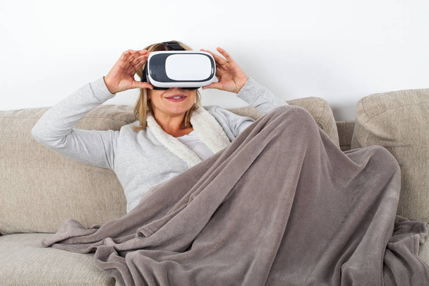 Woman watching a 3d virtual reality video with headset while relaxing on the sofa - Foto, immagini
