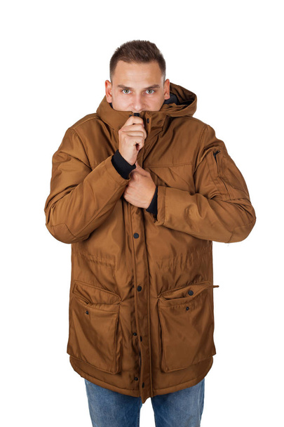 Handsome young man wearing a light brown winter parka jacket - smiling to the camera on isolated background - Zdjęcie, obraz