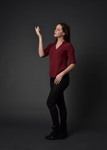 full length portrait of brunette girl wearing  red shirt and leather pants. standing pose , on grey studio background. - 写真・画像