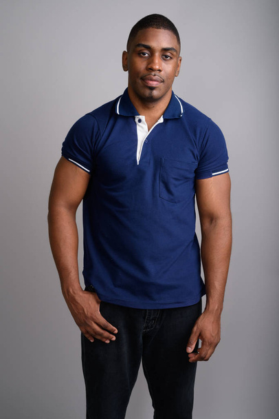 Νεαρό όμορφος Αφρικής άνδρας φοράει μπλε πουκάμισο πόλο ενάντια σε γκρι  - Φωτογραφία, εικόνα