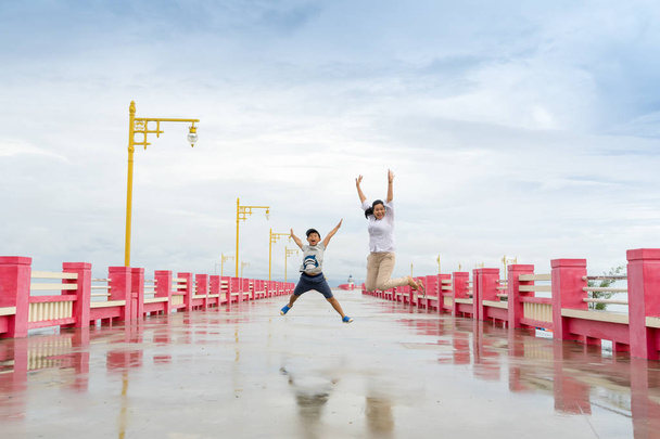 Aasialainen nainen ja pieni poika hyppivät onnesta. Saranin sillalla Prachuap Khiri Khan, Thaimaa
, - Valokuva, kuva
