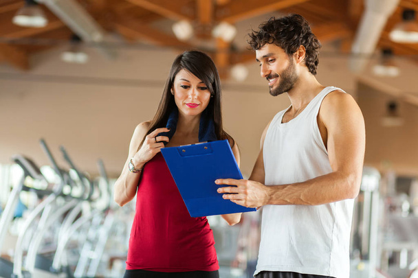 Handsome personal trainer with his client looking at clipboard at the gym - Foto, Imagem