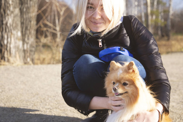 Blonde girl with her dog pet pomeranian spitz (pom) on the path in the wood forest - Foto, Imagem
