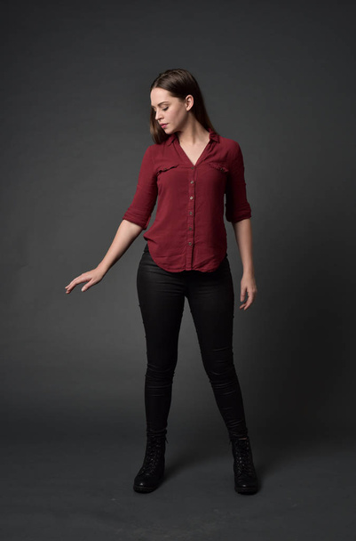 Ganzkörperporträt eines brünetten Mädchens in rotem Hemd und Lederhose. Stehende Pose, auf grauem Studiohintergrund. - Foto, Bild