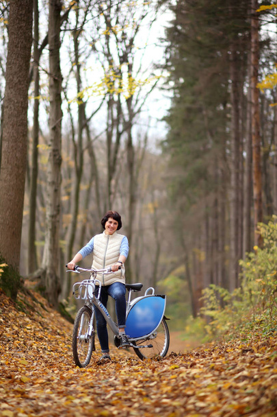 The girl on a bike from the rental in the forest. Beautiful young woman posing for the camera in the autumn forest.  - Fotoğraf, Görsel
