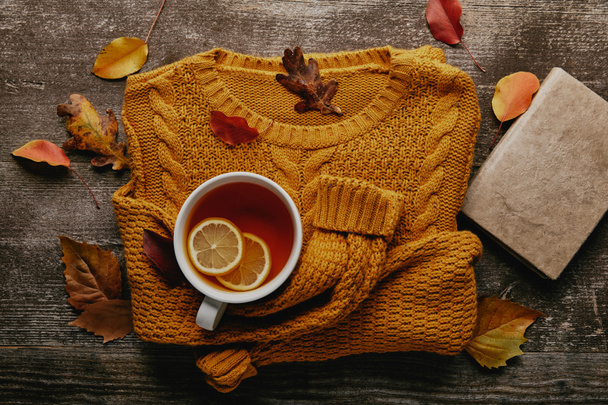 płaskie lay z opadłych liści, filiżanka herbaty z cytryna kawałki, książki i pomarańczowy sweter na drewnianym blatem - Zdjęcie, obraz
