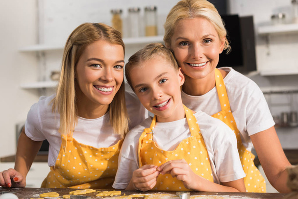adorable happy child with mother and grandmother smiling at camera together in kitchen   - Photo, Image