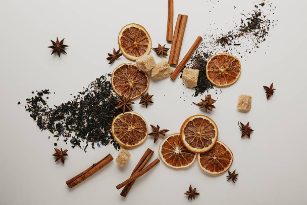 flat lay with arrangement of dried orange pieces, cinnamon sticks, anise stars and brown sugar on white backdrop - Фото, изображение