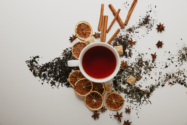 flat lay with arranged cinnamon sticks, anise stars, brown sugar, dried orange pieces and cup of hot tea on white background - Photo, Image
