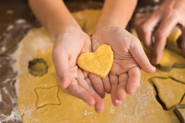 Close-up gedeeltelijke weergave van kind houden hart vormige ongebakken cookie in handen - Foto, afbeelding