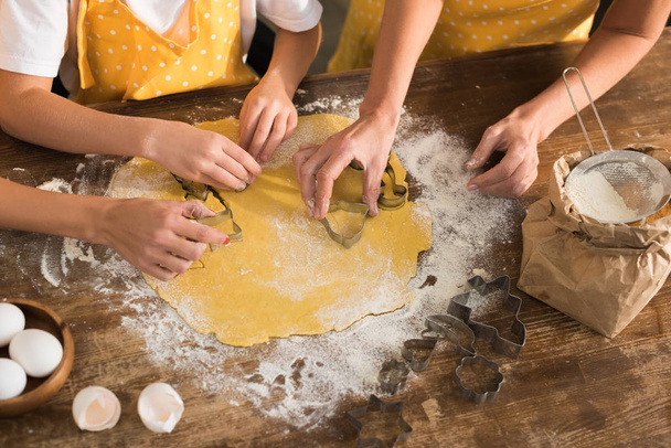 частичный вид ребенка с матерью и бабушкой, готовящих печенье вместе на кухне
   - Фото, изображение