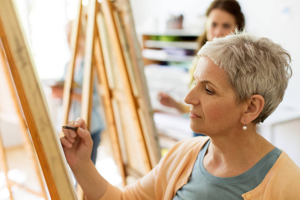 senior woman drawing on easel at art school studio - Foto, afbeelding