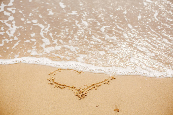 海の近くの波と砂浜に書かれた心。愛の概念。幸せなバレンタインデー。新婚夫婦の新婚旅行。バレンタインの日。テキストのためのスペース。楽しい休暇をお過ごしください。傷ついた心 - 写真・画像