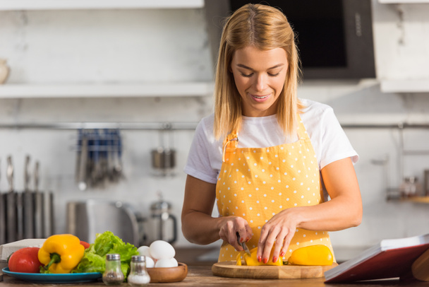 усміхнена молода жінка в фартусі, що ріже овочі на кухні
  - Фото, зображення