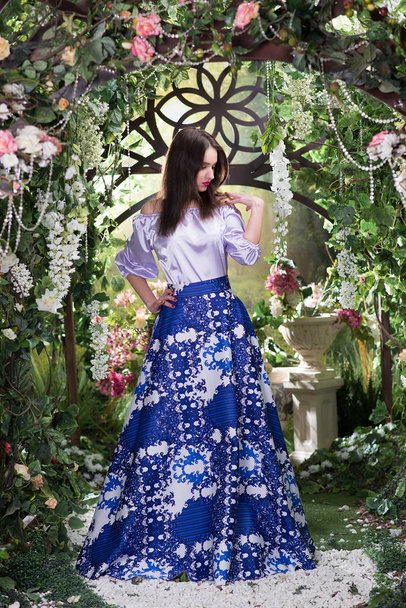 Jeune femme élégante en robe de soie bleue de luxe posant sous une arche fleurie
 - Photo, image