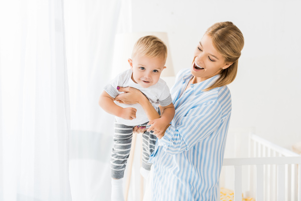 cheerful mother holding toddler in hands in nursery room - Photo, Image