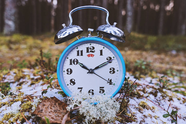 Concept of transition to winter time. Vintage blue alarm clock on winter forest background. Daylight saving time concept winter time - Photo, Image