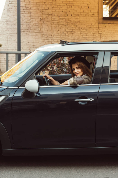 доросла жінка в картатій куртці і чорний капелюх сидить в машині на міській вулиці
 - Фото, зображення