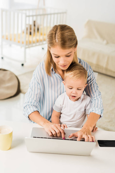 mother sitting at desk with cute toddler while using laptop - Valokuva, kuva