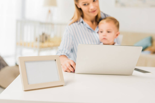 mãe sentada na mesa com a criança bonito ao usar laptop, foco em primeiro plano
 - Foto, Imagem