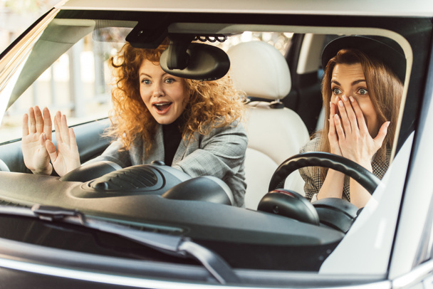 surprised adult female friends gesturing by hands and sitting in car  - Foto, Imagen