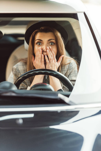 Schockierte Frau gestikuliert mit den Händen, während sie am Steuer im Auto sitzt - Foto, Bild