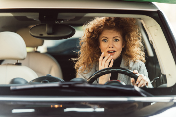 surprised adult ginger curly woman sitting at steering wheel in car - Fotó, kép