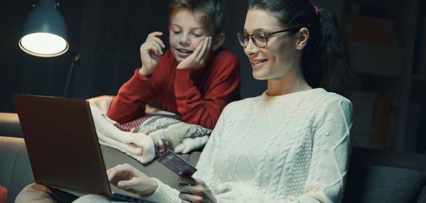 Happy mother and son doing online shopping together using a laptop, she is holding a credit card - Zdjęcie, obraz