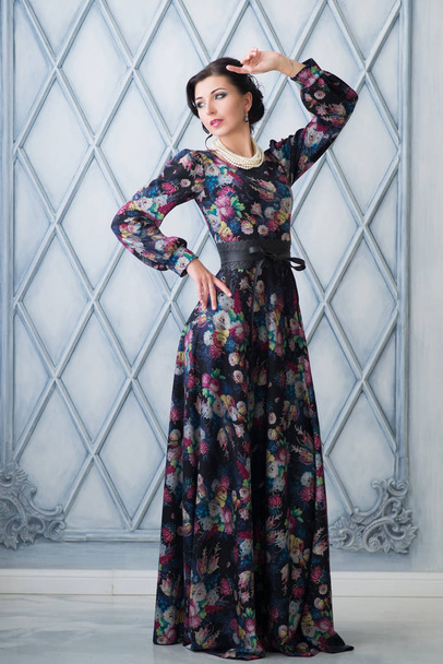 Брюнетка в элегантном платье с цветочным узором позирует в винтажном интерьере
 - Фото, изображение