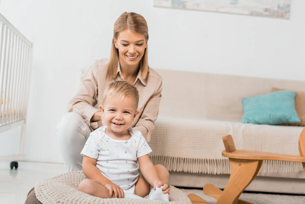 smiling mother and adorable toddler looking at camera sitting in nursery room  - Foto, Bild